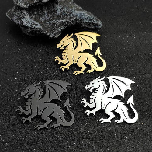 Three dragon-shaped pins in gold, silver, and black on a dark surface.